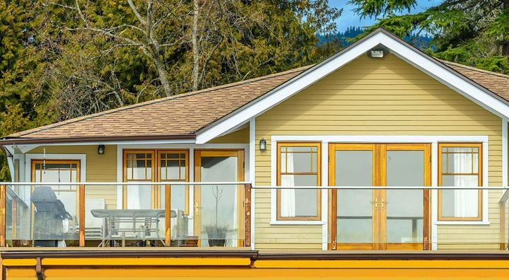 A yellow house with a large balcony and trees in the background.