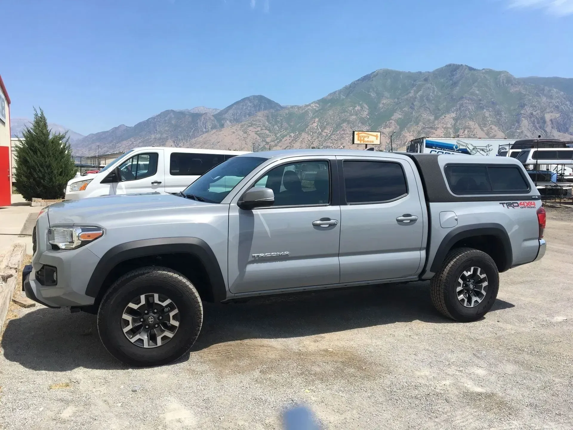 Gray Toyota Tacoma truck with a camper shell parked in front of mountains.