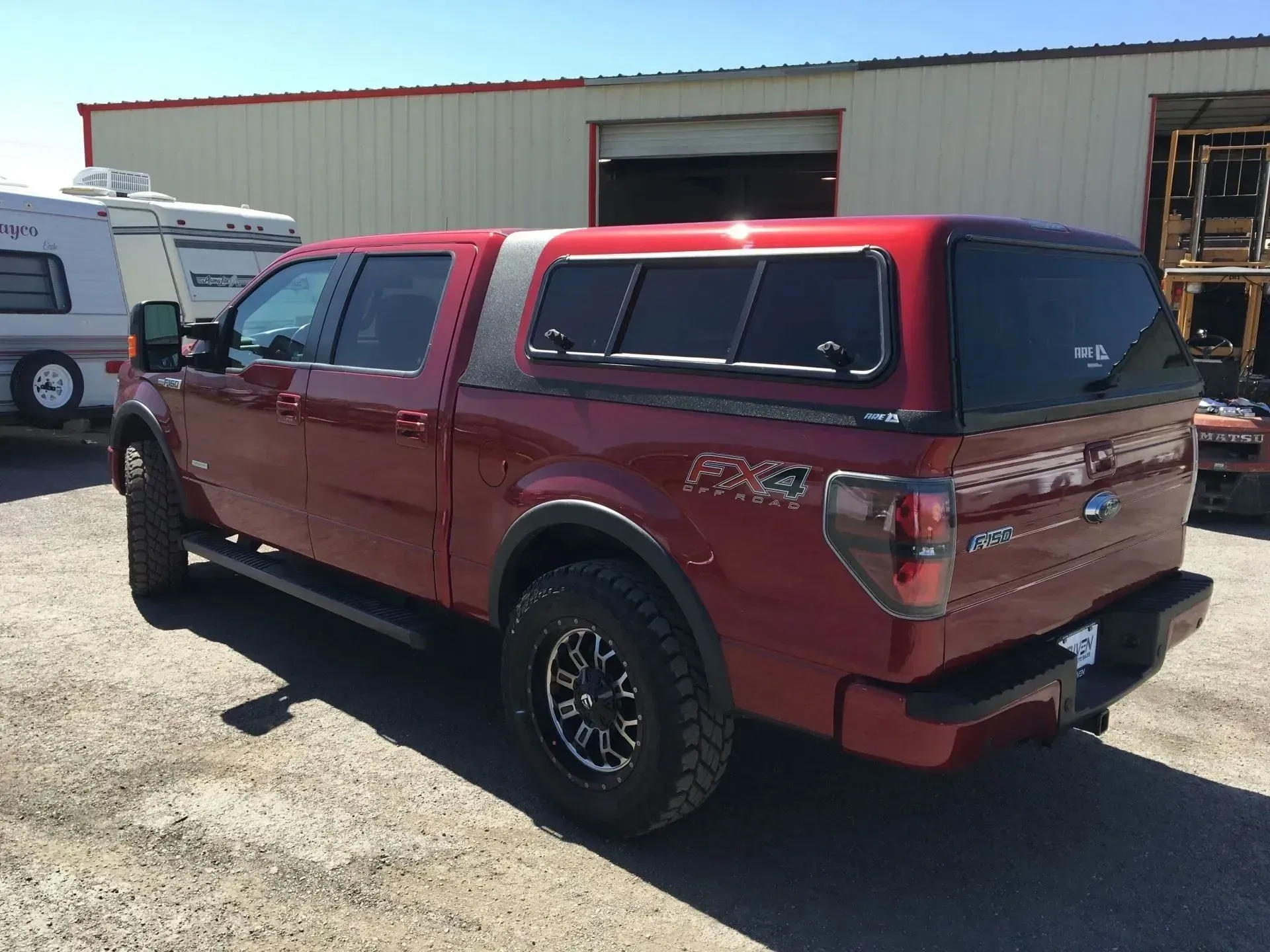 Red Ford F-150 truck with a camper shell, parked outside a building on a sunny day.