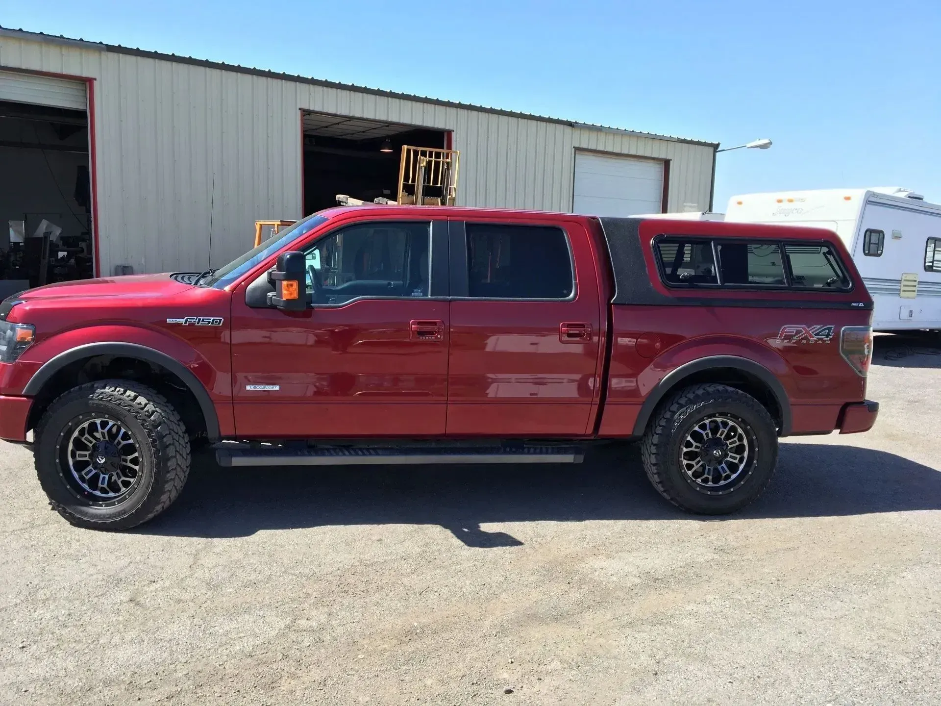 Red pickup truck with black wheels and a matching bed cap parked outside a building.