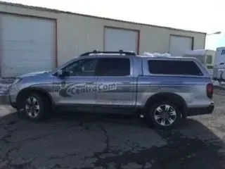 Silver Subaru Baja with a camper shell, parked in front of a building with garage doors. 
