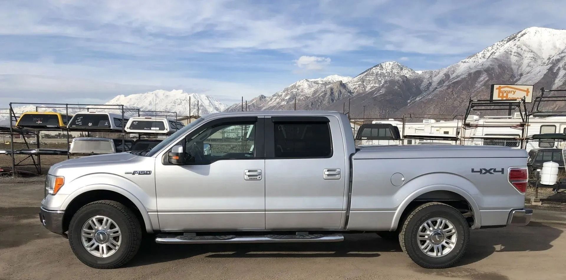 Silver pickup truck parked in front of snow-capped mountains and other vehicles.