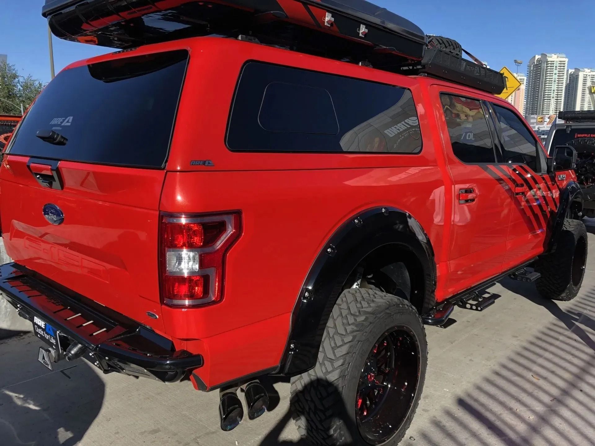Red Ford truck with black camper shell, black wheels, and roof storage.