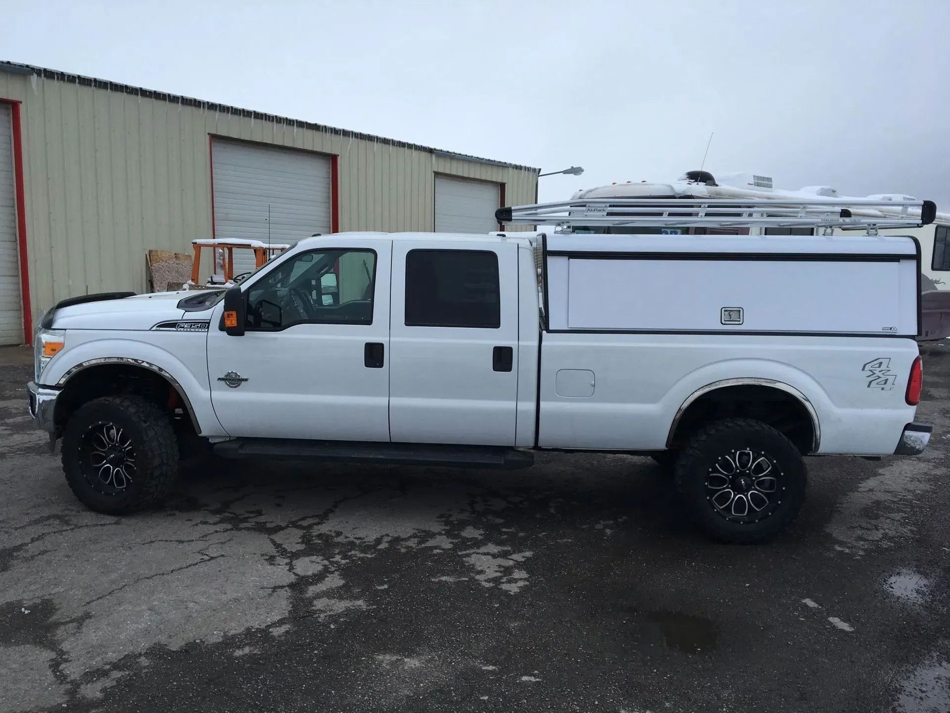 White pickup truck with a cap and roof rack parked in front of a building.