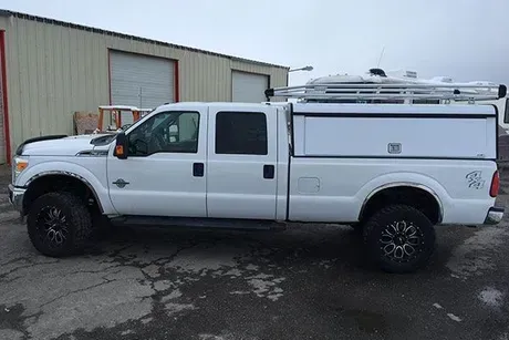 White pickup truck with a utility bed, rack, and black wheels parked outside a building.