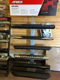 Display of various black and silver side bars for trucks and cars, mounted on a rack with Aries branding.