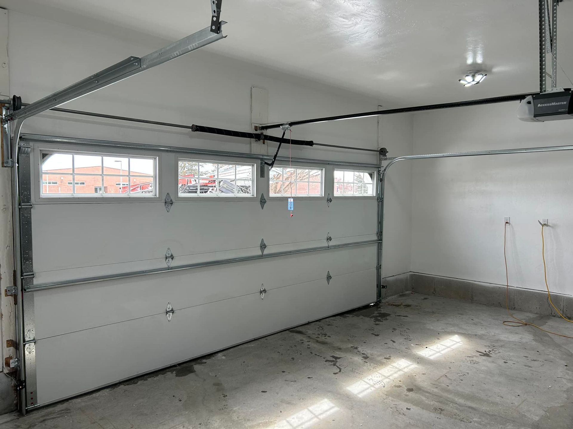 White garage door partially open, interior view. Concrete floor, white walls, and windows at top.