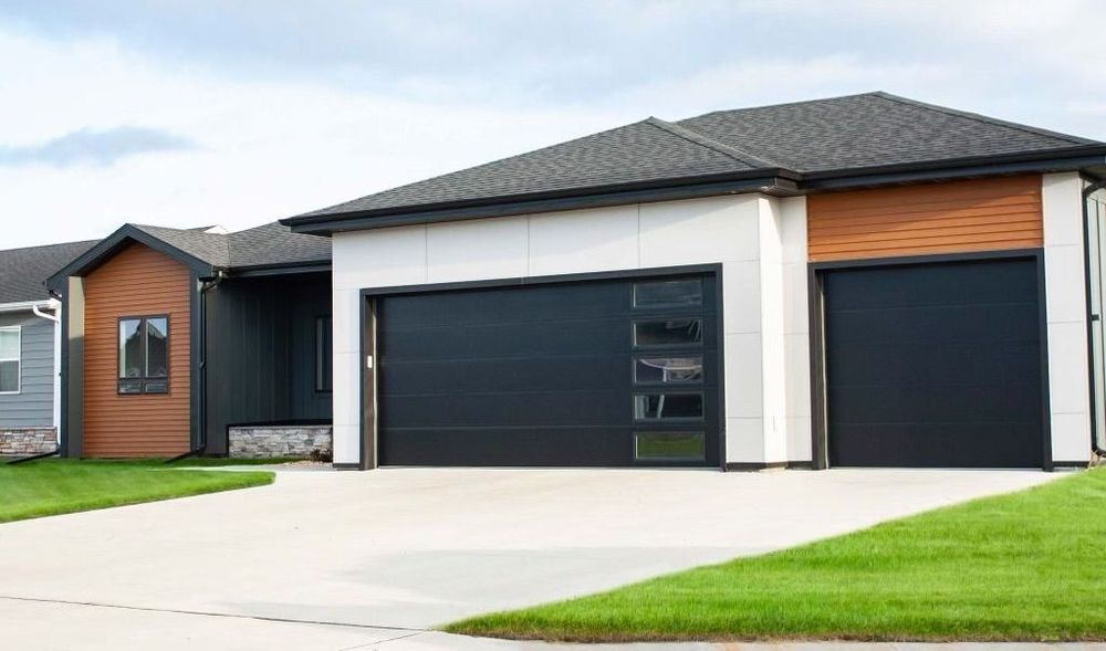 Modern home with black garage doors, wood accents, and a concrete driveway.