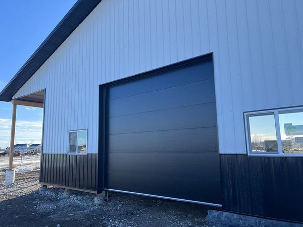 Black and white metal building with a large black garage door. Two small windows on the right.