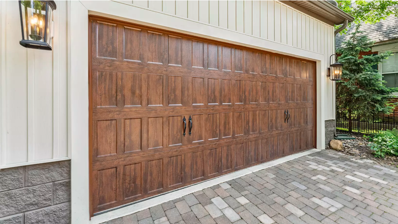 Brown garage door with decorative panels; brick driveway, white trim, and lanterns.