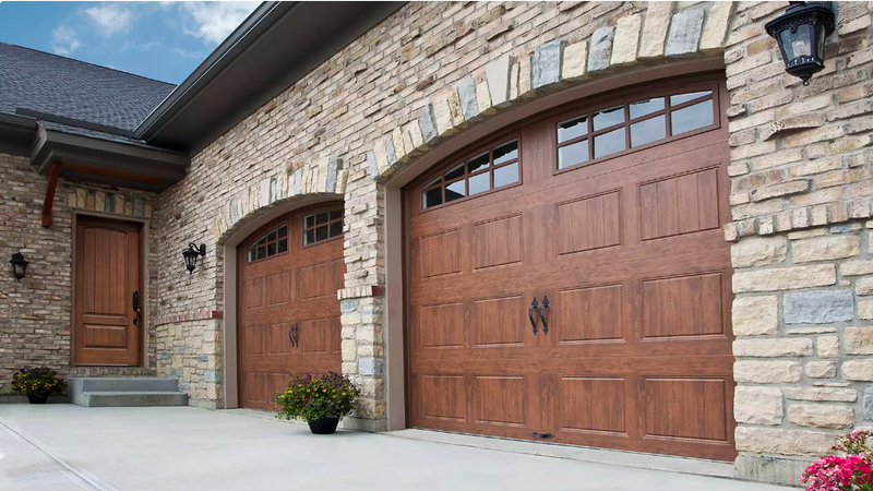 Brown garage doors with arched tops, stone facade, and a wooden front door.
