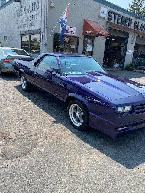 A purple car is parked in front of a car dealership.
