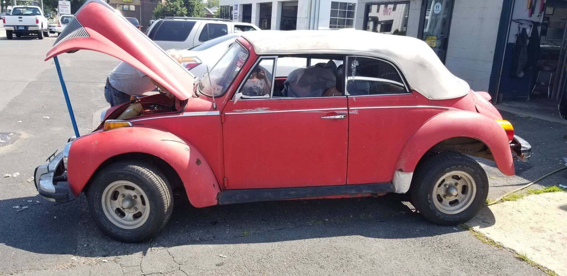 A red car with the hood up is parked on the side of the road