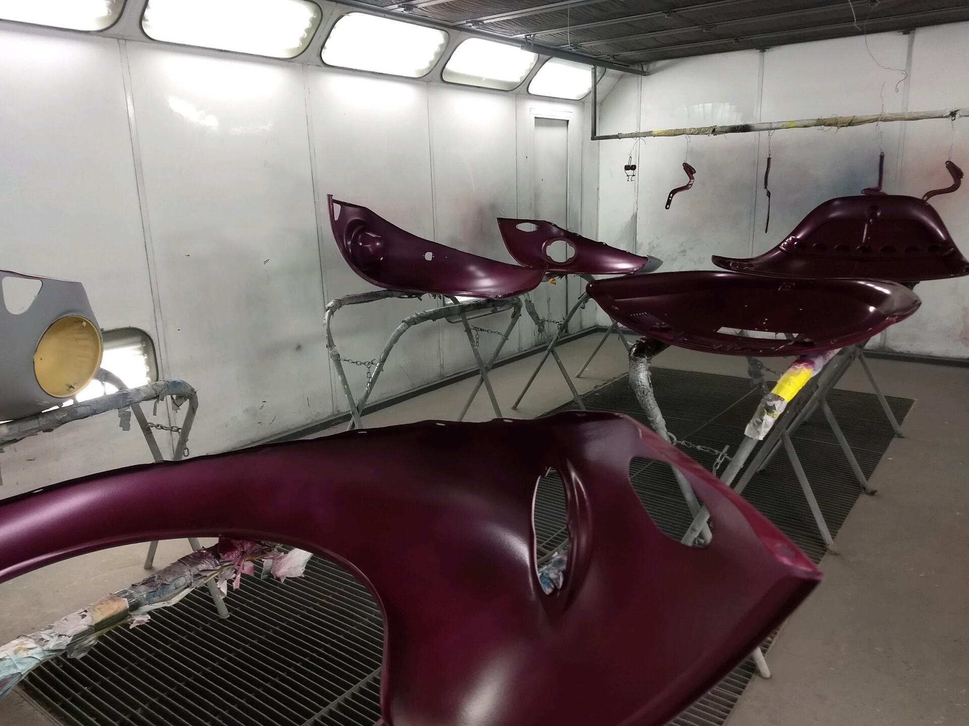 A purple car is being painted in a paint booth