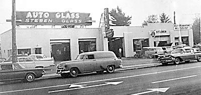 A black and white photo of cars parked in front of an auto glass store.