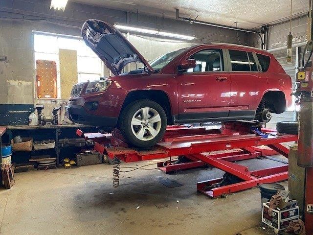 A red jeep is sitting on a lift in a garage.