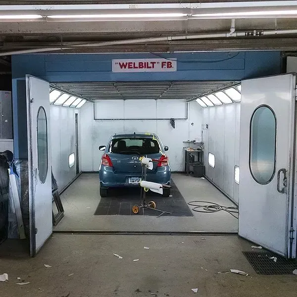 A car is parked in a paint booth with a welbilt fb sign above it.