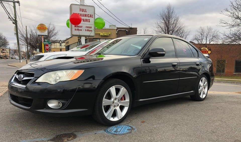 A black car is parked on the side of the road in front of a building.