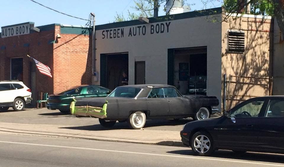 A black car is parked in front of a steben auto body