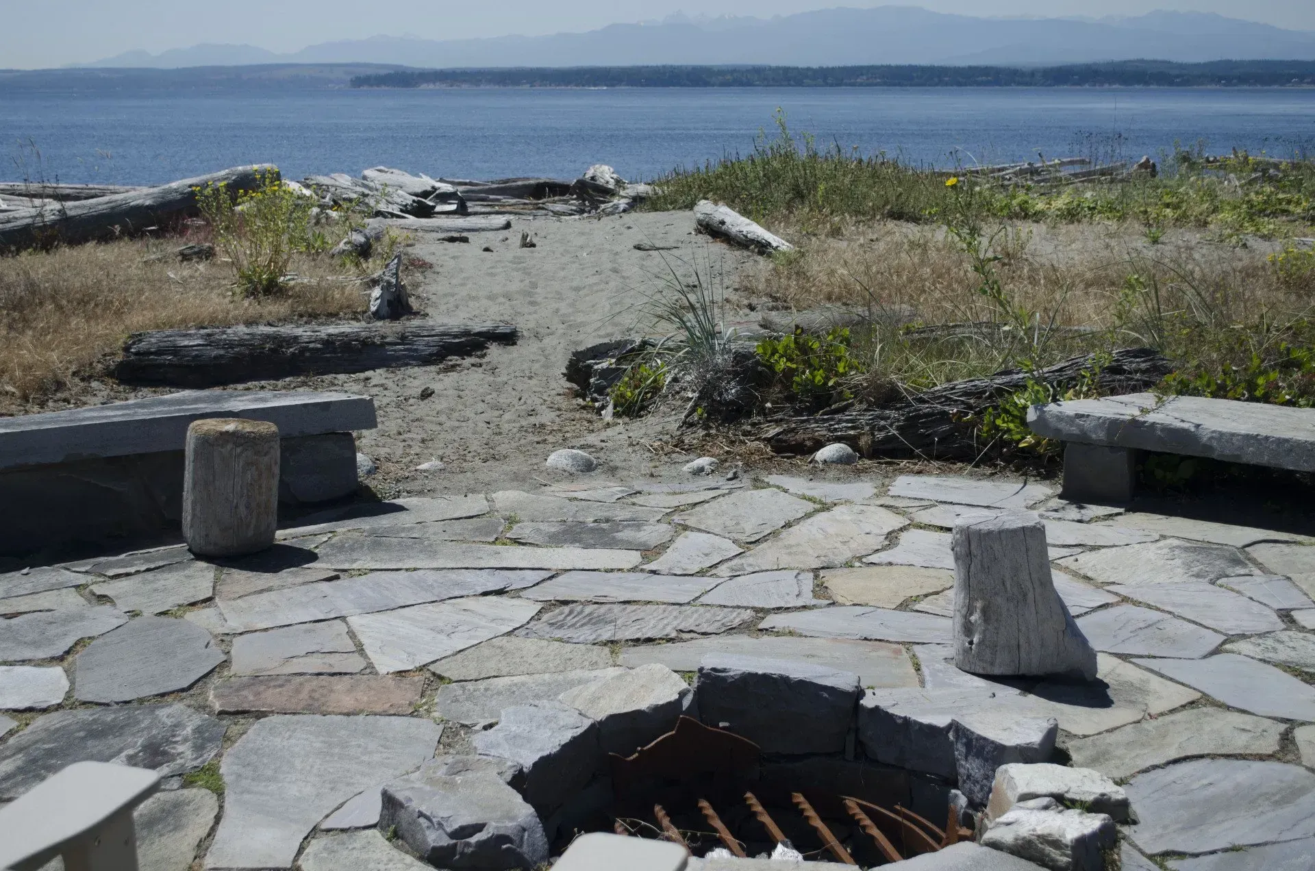 Stone fire pit with benches overlooking a bay and distant mountains.