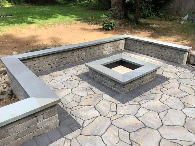 Stone patio with built-in fire pit and low retaining walls, in a backyard setting.