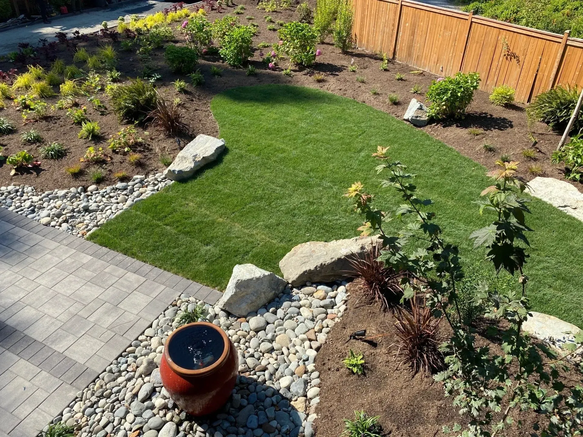A well-landscaped garden with grass, rocks, plants, and a brick pathway.