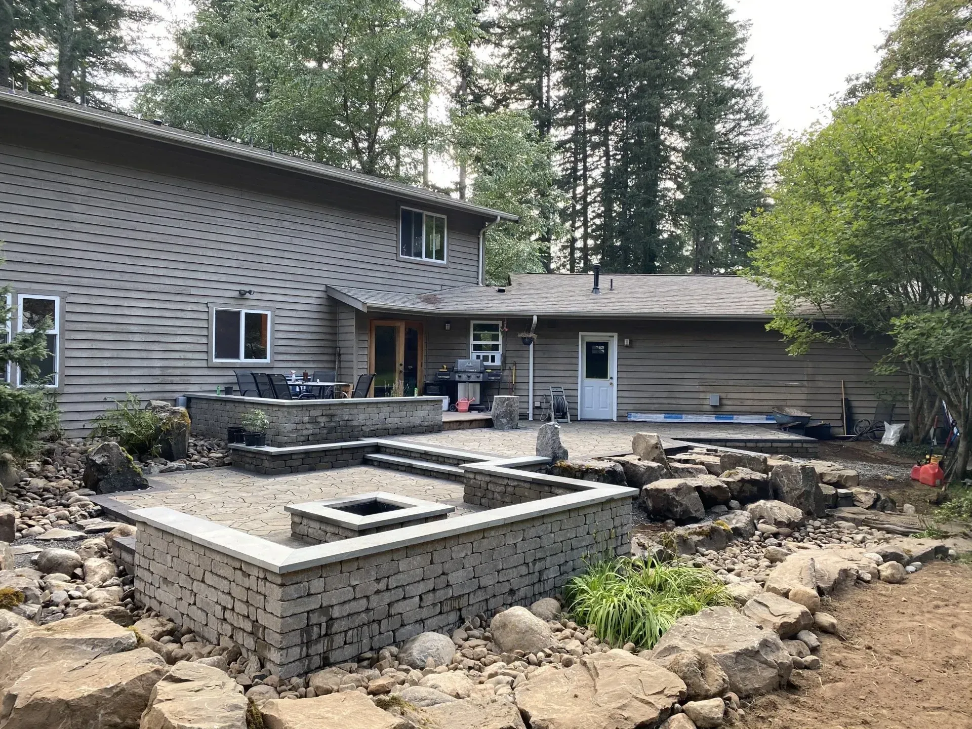 Backyard with a two-story house and newly constructed stone patio with fire pit and retaining walls.