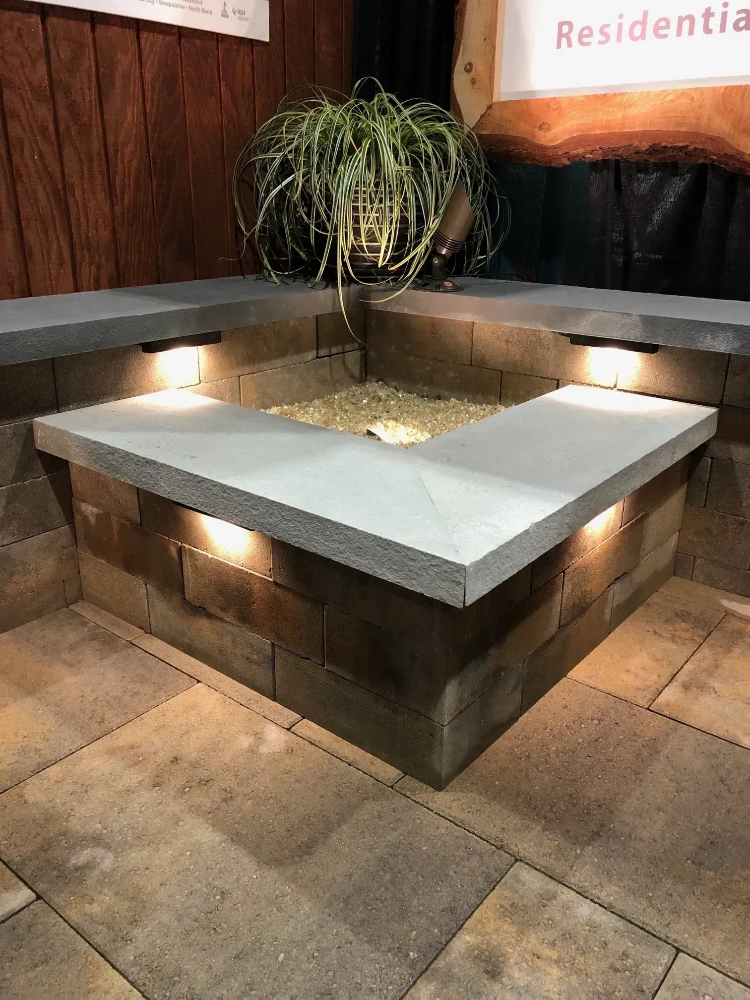 Stone-walled outdoor fire pit with built-in lights and a potted plant, surrounded by stone paving.