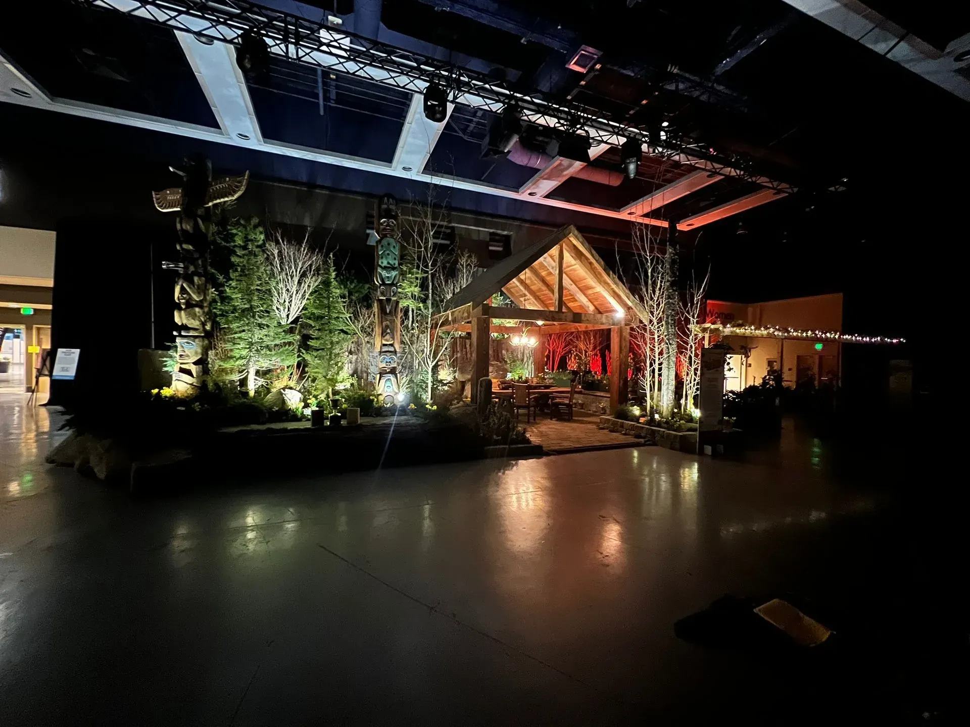 Stage set: rustic cabin, trees, and warm lighting in a large, dark space.