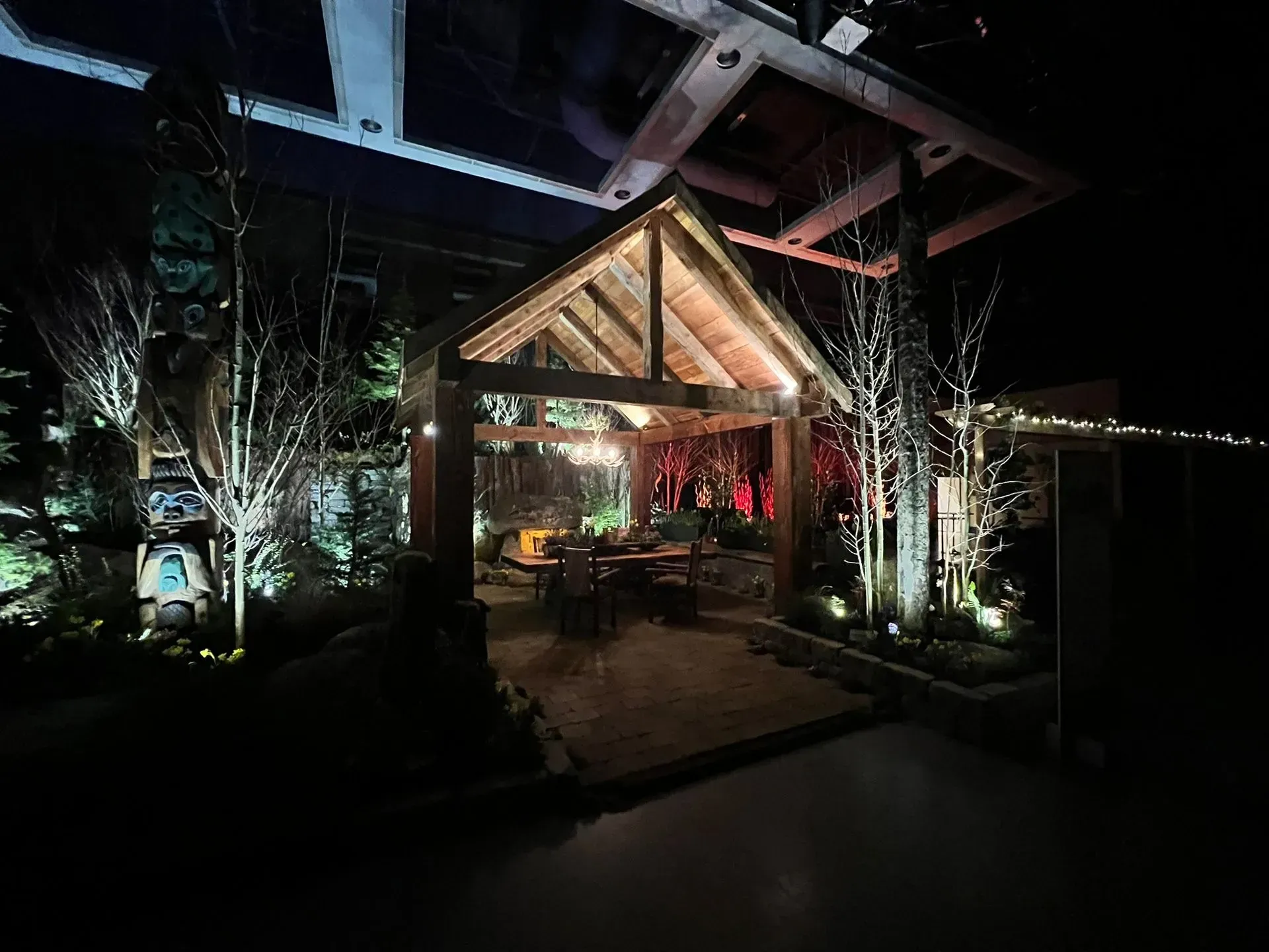 Wooden gazebo lit at night with trees and a table setting inside.