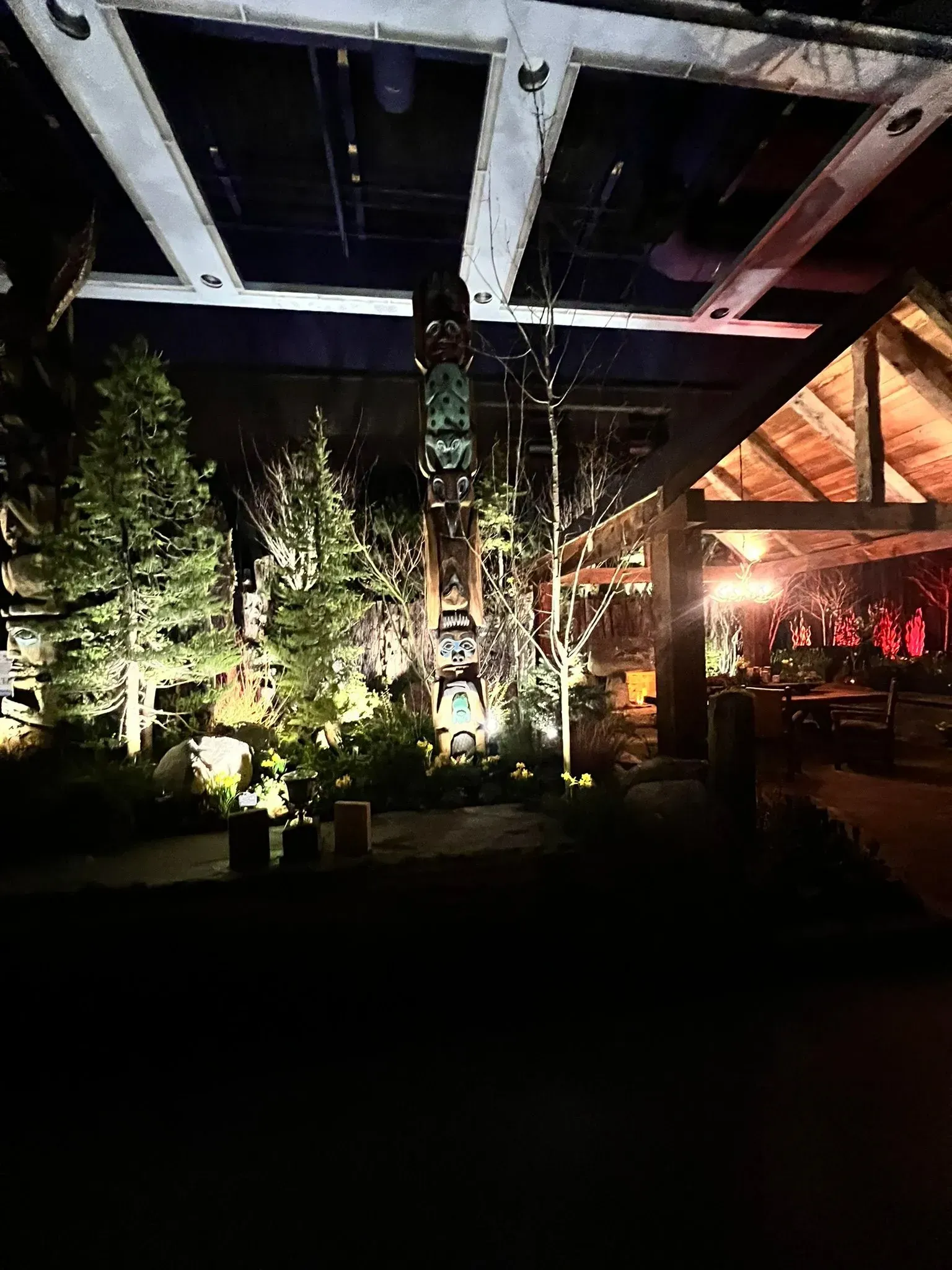 Nighttime scene with illuminated trees, totem pole, and wooden structure under a dark ceiling.
