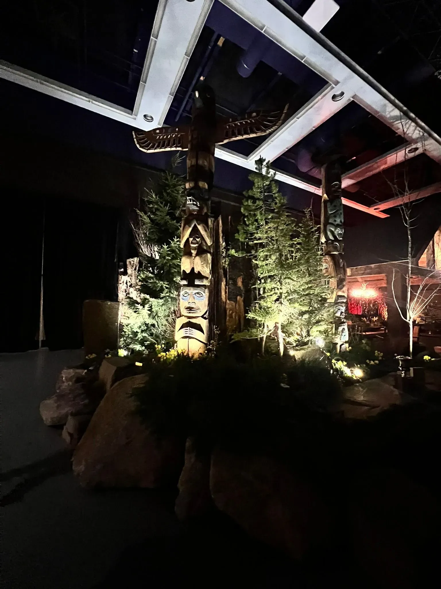 Totem poles and trees illuminated indoors, with dark rocks and low lighting.