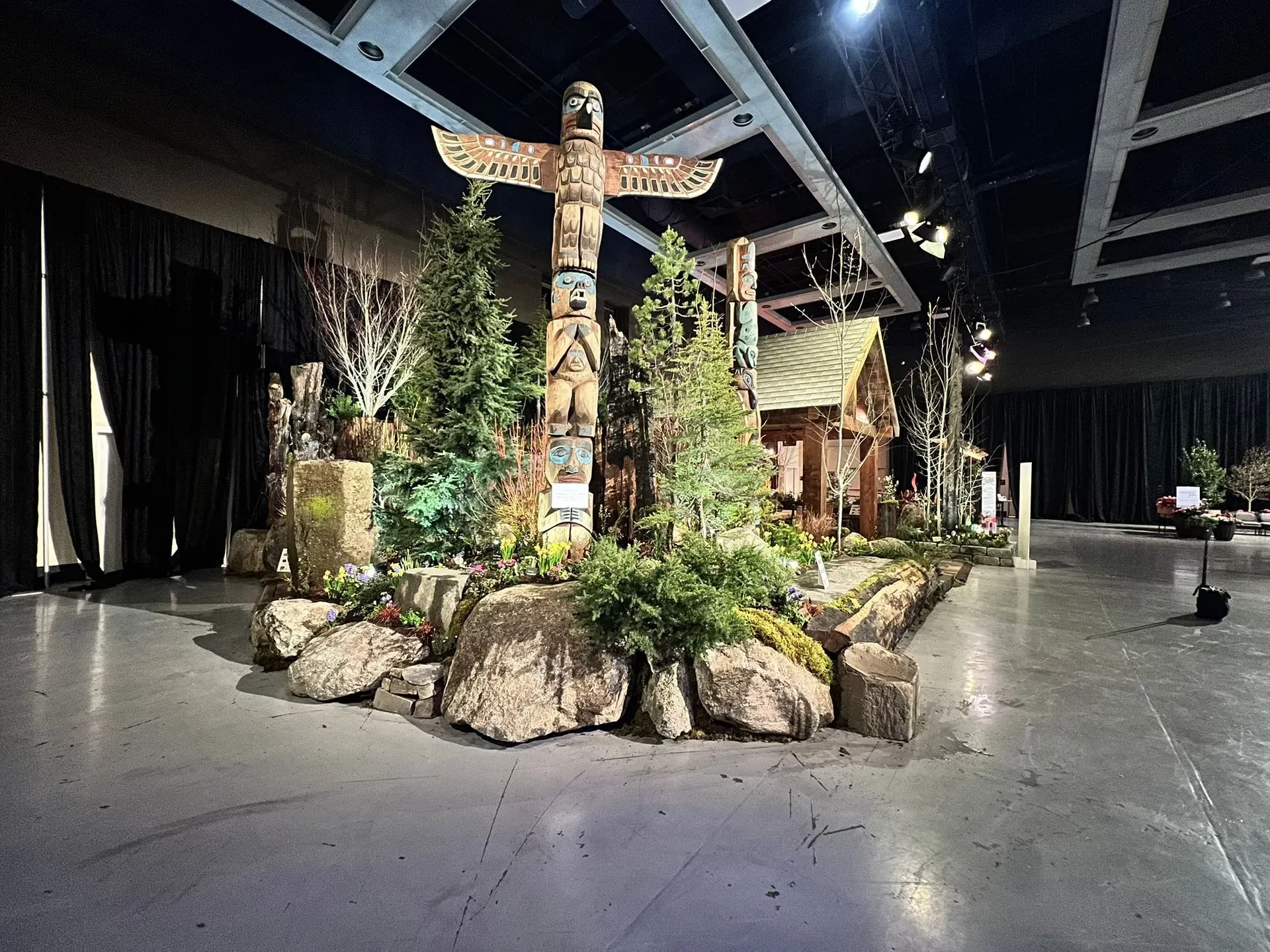 Totem pole display with a cabin, trees, and large rocks indoors.