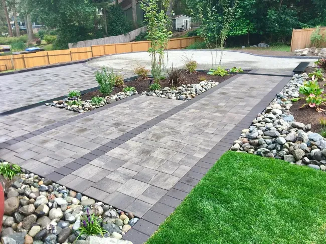Driveway with pavers, rock borders, and green grass.
