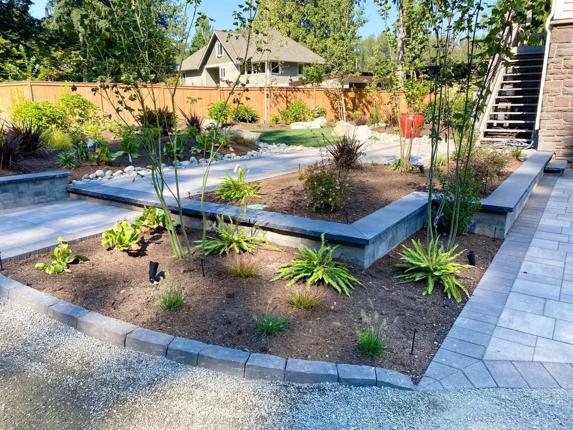 Landscaped backyard with stone patio, retaining walls, and planted beds.