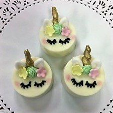 Three cupcakes with unicorn faces on them are sitting on a white plate.
