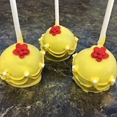 Three yellow cake pops with red flowers on top are sitting on a table.