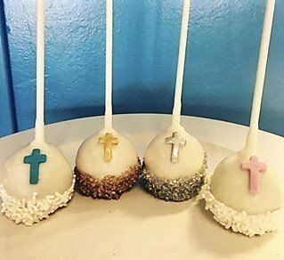 Four cake pops with crosses on them on a white plate