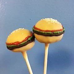 Two hamburger cake pops on sticks on a blue background.