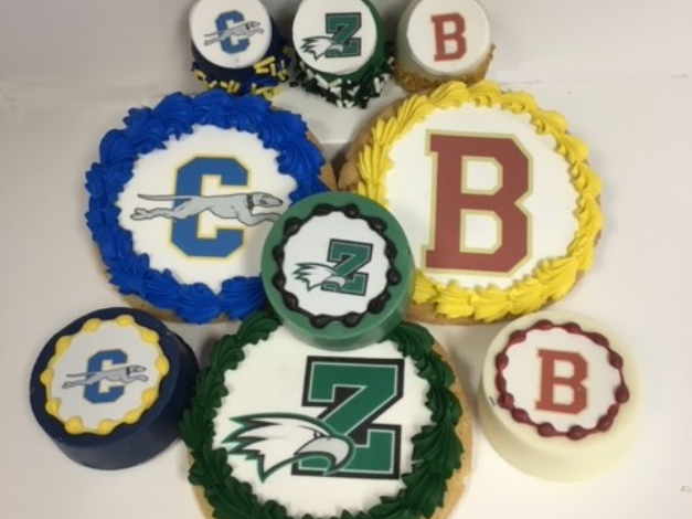Assorted blue, green, yellow, and red cookie or cake pops decorated with lettered sports team logos.
