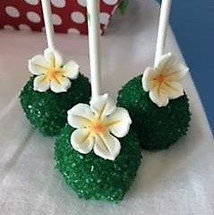 Three green cake pops with white flowers on them on a table.