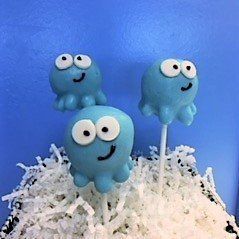 Three blue octopus cake pops are sitting on top of a pile of shredded coconut.