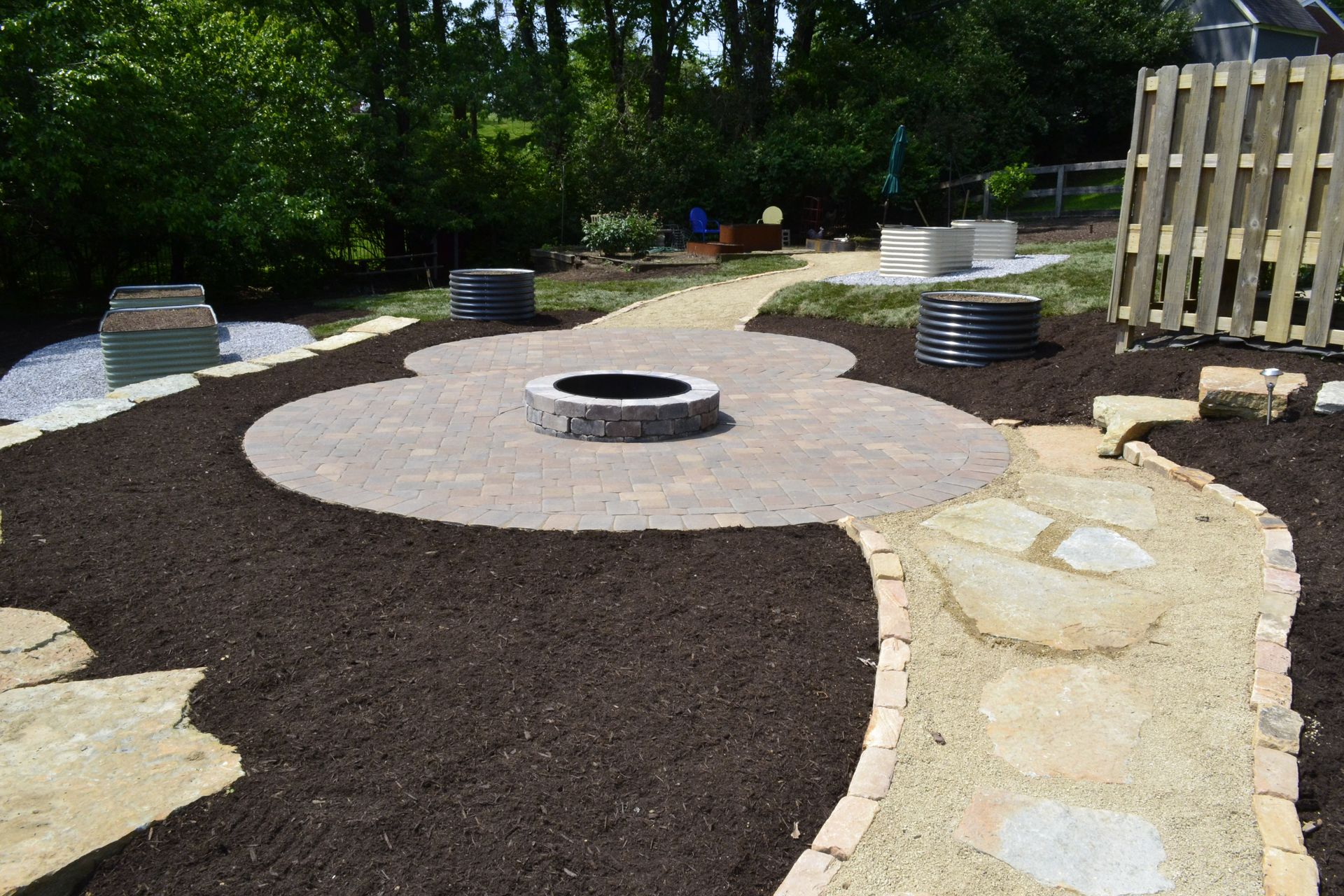 A fire pit is in the middle of a patio in a backyard.