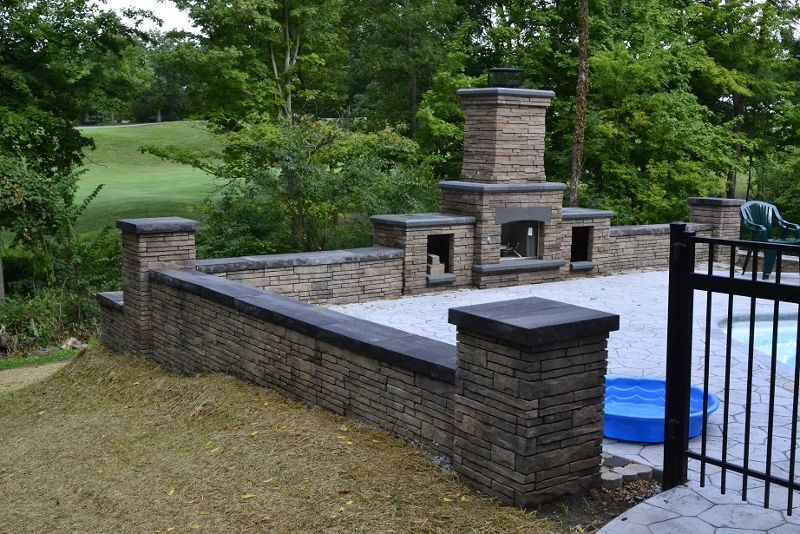 A brick wall surrounds a patio with a fireplace and a pool.