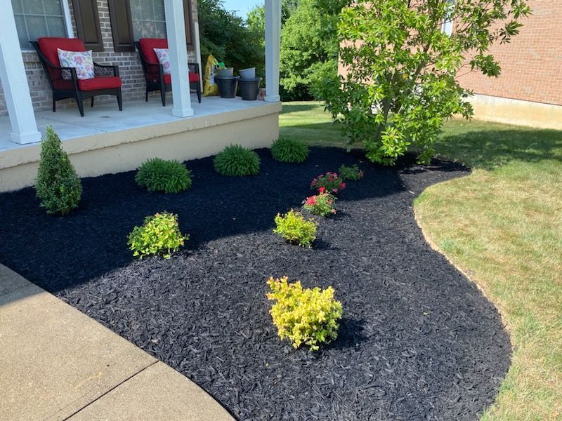 A house with a porch and a lawn with black mulch and plants.