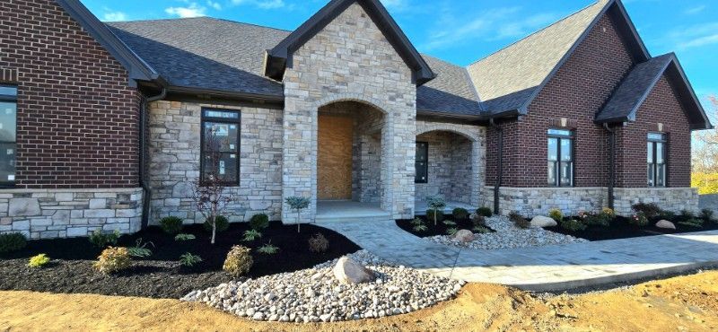 A large brick and stone house with a large driveway in front of it.