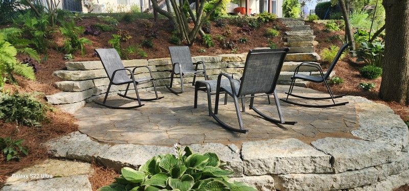 A group of rocking chairs sitting on top of a stone patio.
