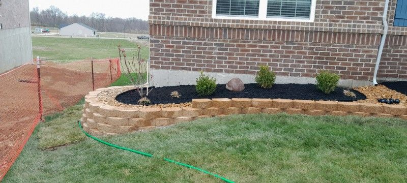A brick house with a garden in front of it and a green hose.