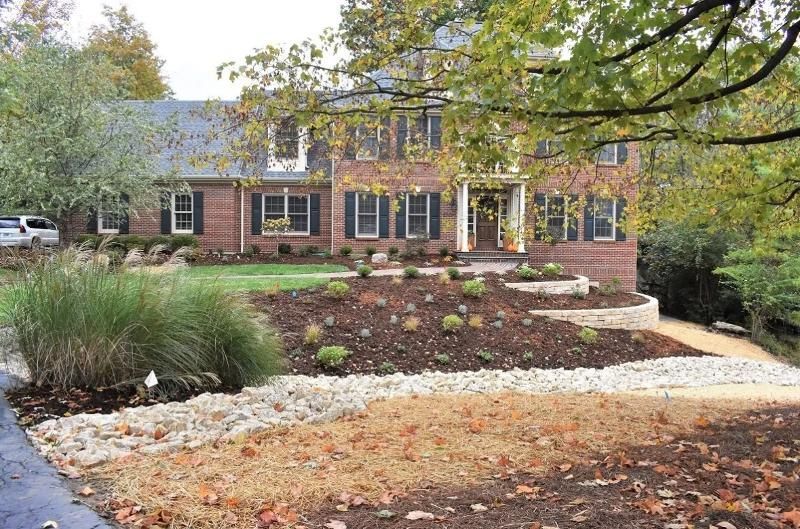 A large brick house with a lush green lawn and a driveway leading to it.
