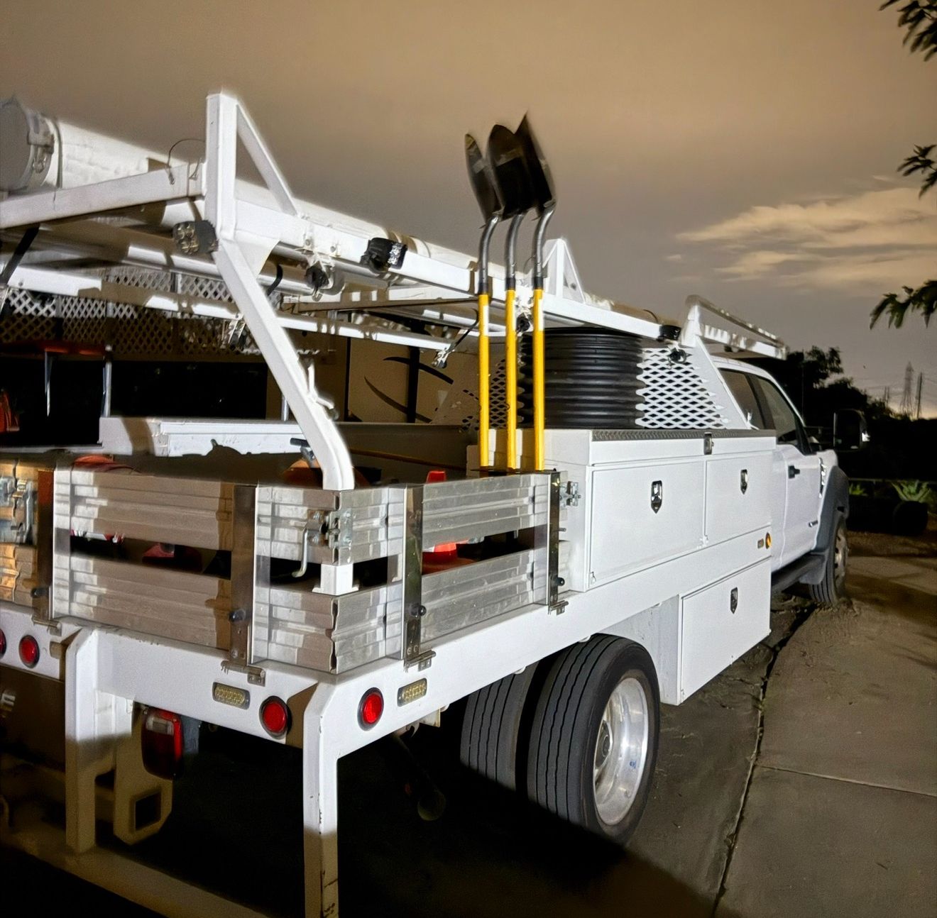 White utility truck with ladders and stacked materials parked on a street at dusk